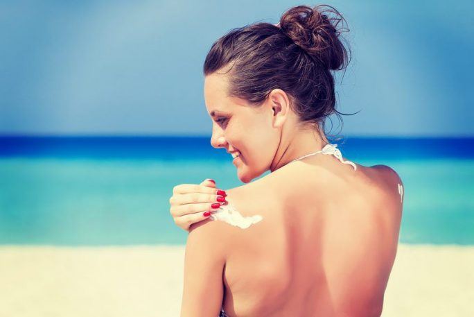 A smiling woman is applying sunblock on the beach